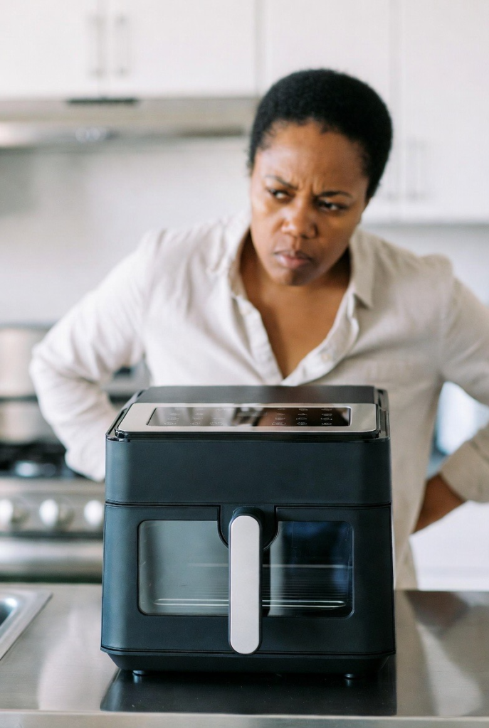 A lady with frustrated face standing behind an air fryer